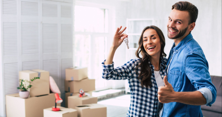 couple tenant les clefs de leurs nouveau logement, avec leurs cartons de déménagement en fond